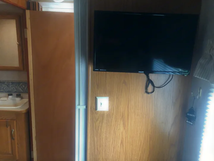 RV rental interior: wood-paneled wall with a Philips TV, a compact bathroom sink, and a space-saving sliding door.. Damon Daybreak 2005
