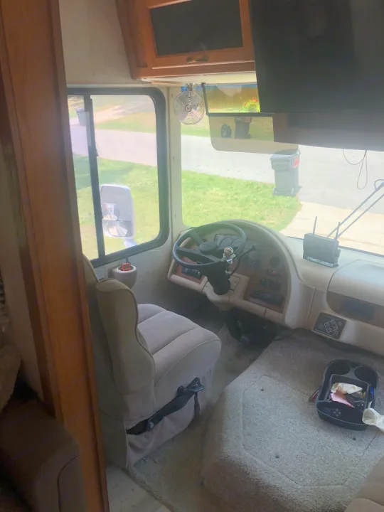 View inside an RV rental's spacious cockpit, featuring the driver's seat, steering wheel, and dashboard with a clear front view.. Damon Daybreak 2005