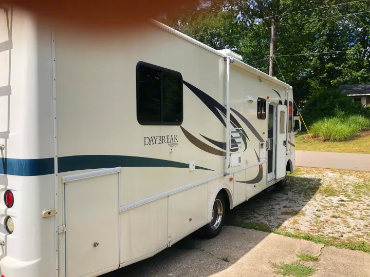 This white Damon Daybreak motorhome, perfect for an RV rental, is parked outdoors. Side view reveals windows, compartments, and open entry.. Damon Daybreak 2005