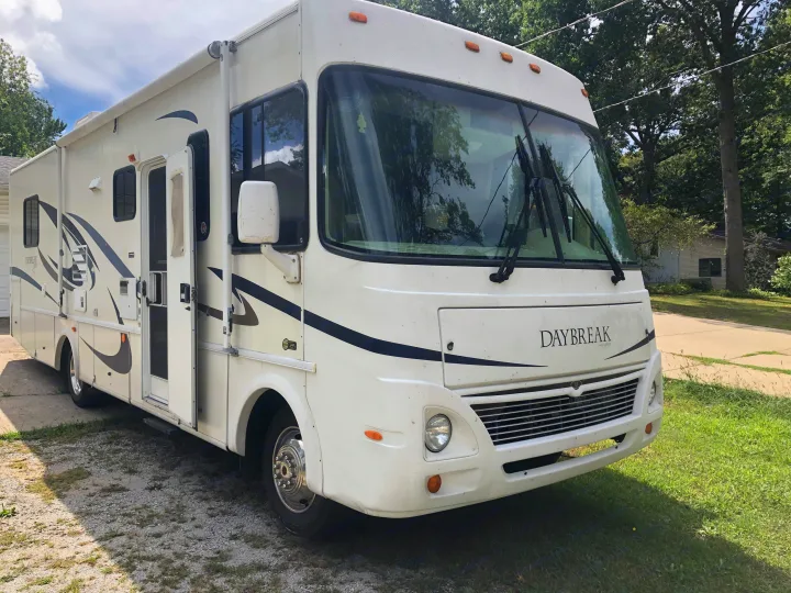 This white Daybreak motorhome, ready for rv rental, is parked on a gravel drive with trees in the background.. Damon Daybreak 2005