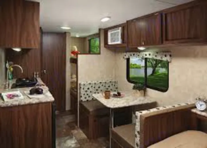 This RV rental interior shows a compact kitchen, dinette, and bunk beds. Scenic lake views from windows, dark wood cabinets.. Coachmen Clipper 2016