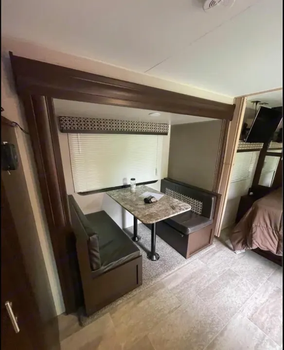 RV rental interior featuring a compact dining booth with table, window, and adjacent bedroom area.. K-Z Manufacturing Sportsmen 2019