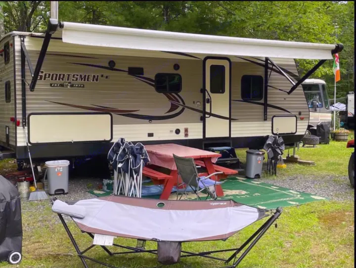 Spacious RV rental campsite with an extended awning, picnic table, and hammock, offering a relaxing outdoor retreat.. K-Z Manufacturing Sportsmen 2019