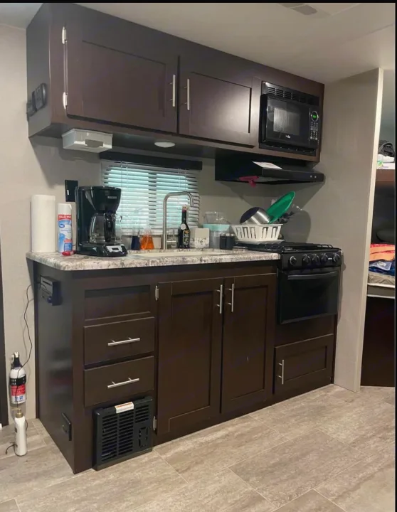 Compact and functional RV kitchen with dark cabinets, a stove, microwave, and sink, perfect for your next rv rental adventure.. K-Z Manufacturing Sportsmen 2019