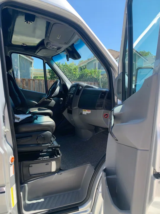 This RV rental's bright front cabin interior, showing the driver and passenger seats, dashboard, and open door.. Roadtrek Agile Ss 2019