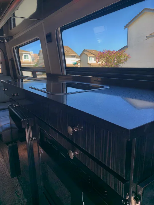 Sleek RV rental interior features a dark kitchen countertop with a sink, modern cabinets, and a scenic window view.. Roadtrek Agile Ss 2019
