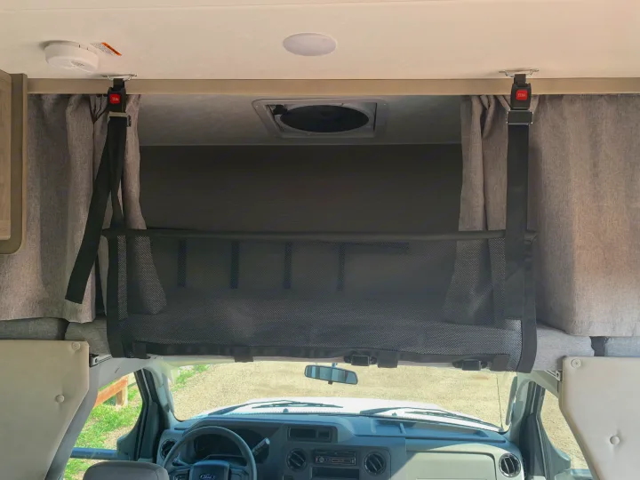 Inside an RV rental, a black mesh safety net spans the overhead bunk, secured by red-buckled straps, with a smoke detector above.. Other Other 2021