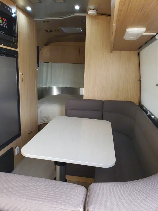 Modern rv rental interior showing a compact kitchen, dining area with U-shaped seating & table, leading to a cozy bedroom.. Airstream Flying Cloud 2020