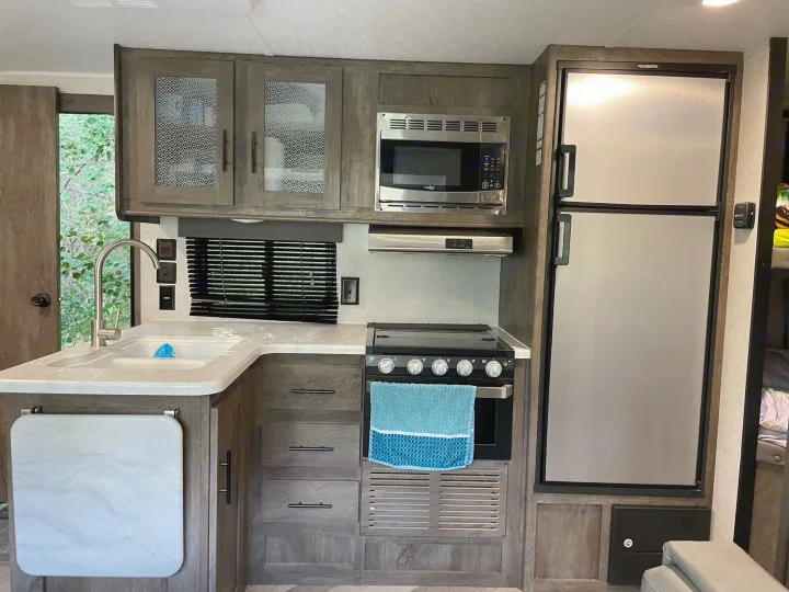 This modern RV rental kitchen showcases a compact setup: sink, microwave, stove, and fridge.. Forest River Wildwood X-Lite 2020