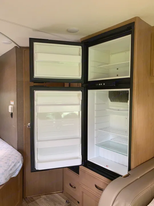 Interior of an RV rental with an open, empty refrigerator and freezer, highlighting built-in kitchen and living space features.. Thor Four Winds 2019