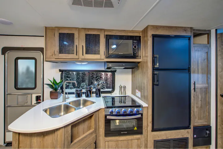 Compact, modern RV rental kitchen with dual sink, microwave, stove, and fridge. Perfect for your next adventure.. Heartland RVs Pioneer 2021