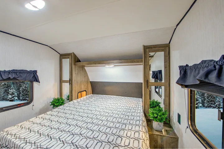 Cozy RV rental bedroom with patterned bed, windows showing snowy forest, and ambient lighting. Perfect for winter adventures.. Heartland RVs Pioneer 2021
