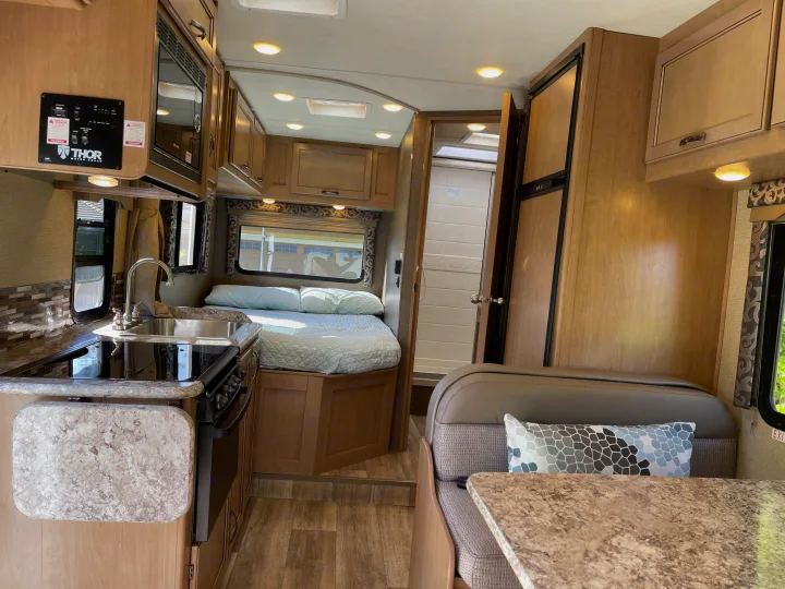 An RV rental's practical interior: full kitchen, comfortable bed, dinette, and shower.. Thor Four Winds 2019