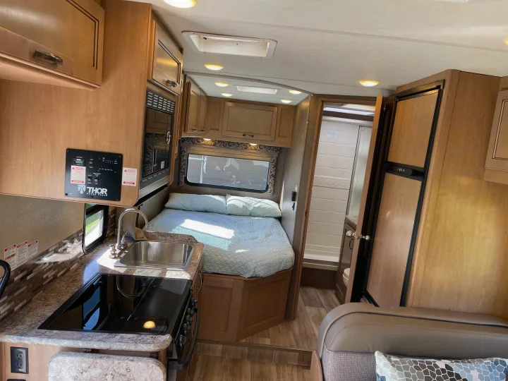 Interior of an rv rental showing a compact kitchen, comfortable bed area, and private bathroom with shower. Ready for your travels!. Thor Four Winds 2019