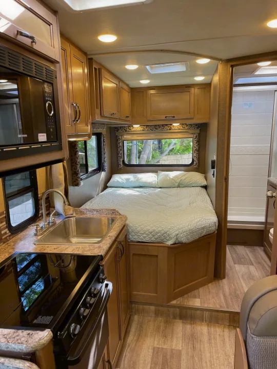 Cozy RV rental interior showcasing a compact kitchen, comfortable bedroom, and accessible shower for a great travel experience.. Thor Four Winds 2019