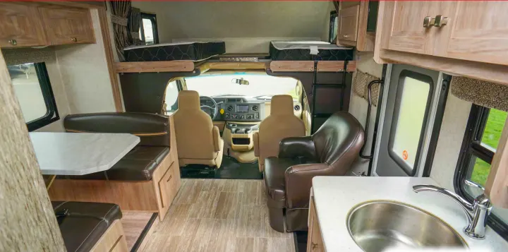 Interior of an RV rental showing the cockpit, an overhead bunk bed, a dinette, and a kitchen sink, highlighting its spacious design.. Forest River Sunseeker 2019