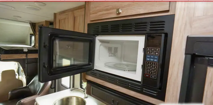 RV rental kitchen: An open microwave is centered, with a sink to the left and an overhead bunk visible.. Forest River Sunseeker 2019