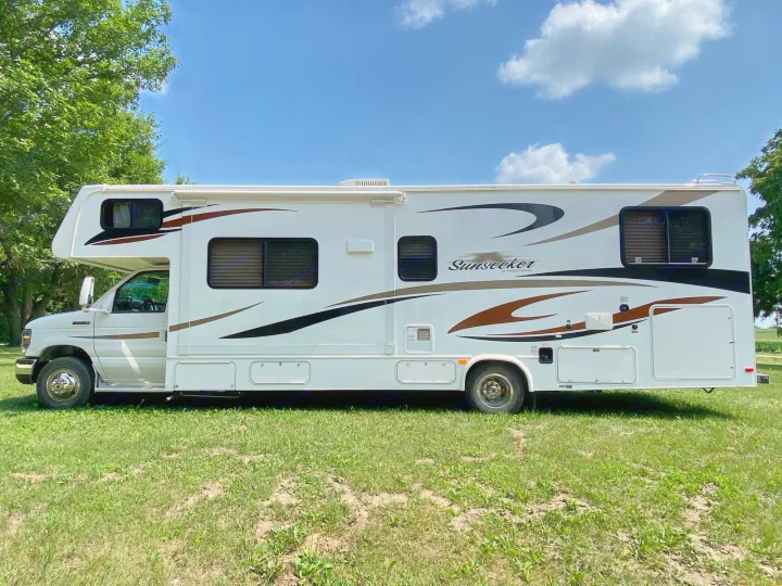 A white Forest River Sunseeker RV rental is parked on green grass under a clear blue sky, ready for your next adventure.. Forest River Ford Sunseeker 2013
