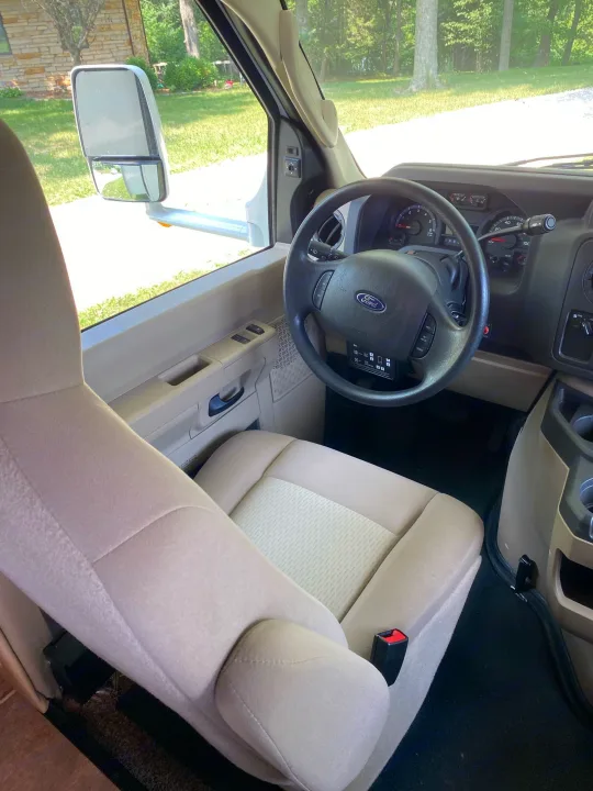 Bright RV rental cockpit view. Shows the dashboard, steering wheel, passenger seat, and large side mirror.. Forest River Ford Sunseeker 2013