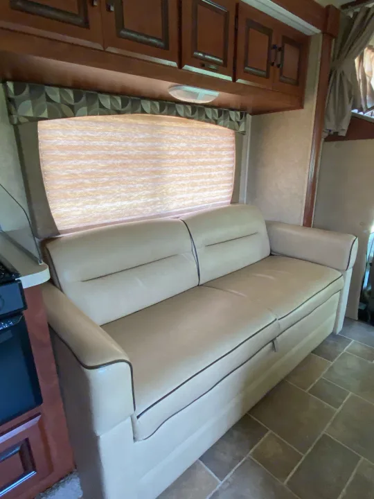 Inside this RV rental: a light-colored sofa, window with a pleated shade, wood cabinets, and tiled floor provide comfort.. Forest River Ford Sunseeker 2013