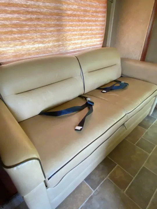 Light-colored sofa with black seatbelts in an RV rental interior. Features pleated blinds and tiled floor for comfy travel.. Forest River Ford Sunseeker 2013