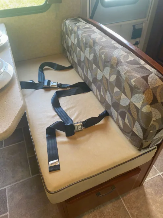 RV rental dinette with beige bench cushion, patterned back cushion, and two black seatbelts, ready for travel.. Forest River Ford Sunseeker 2013