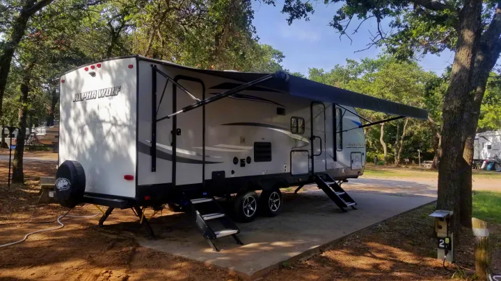 Shaded RV rental at a campsite. This Alpha Wolf travel trailer has its awning out and steps down.. Forest River Cherokee Alpha Wolf 2020