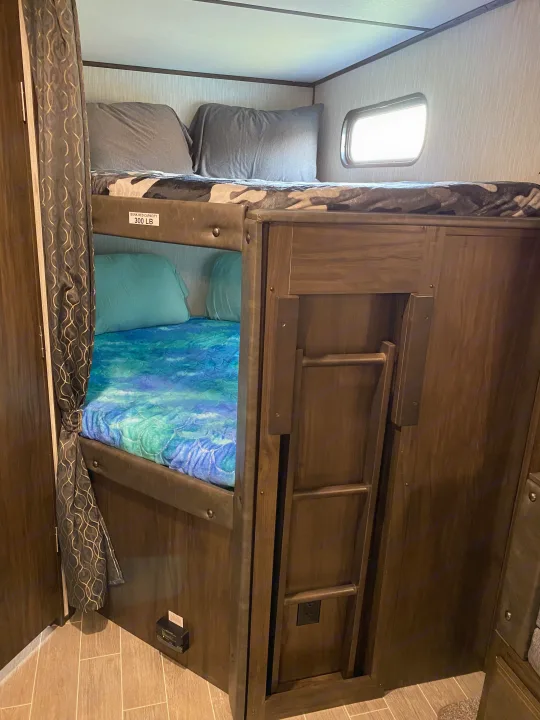 Inside an RV rental: two cozy bunk beds with different bedding designs and an attached ladder, ideal for family camping.. Forest River Cherokee Alpha Wolf 2020