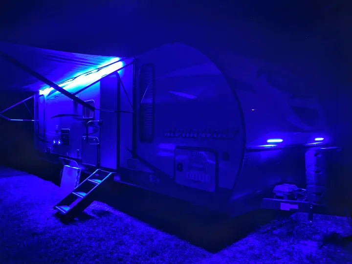 A striking Alpha Wolf travel trailer RV rental at night, illuminated by vibrant blue LED lights under its awning and on the front.. Forest River Cherokee Alpha Wolf 2020