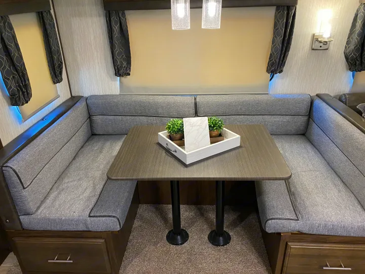 Cozy RV rental dinette featuring U-shaped gray upholstered seating, a wooden table with decor, and bright overhead lights.. Forest River Cherokee Alpha Wolf 2020