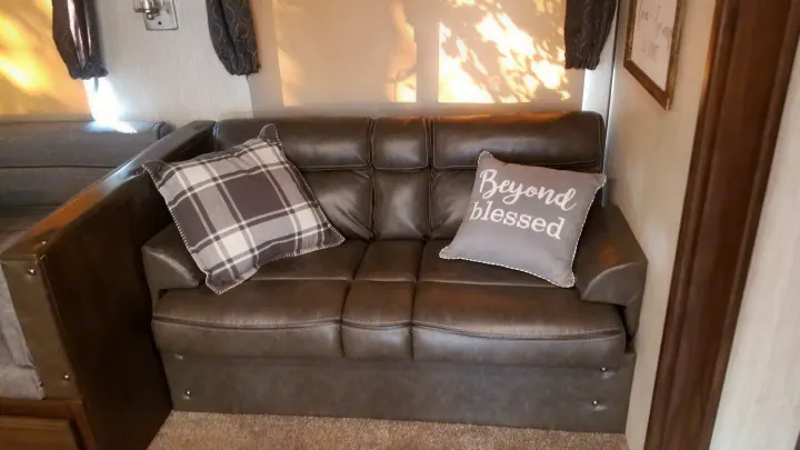 Plush RV rental interior featuring a comfortable sofa with plaid and "Beyond Blessed" pillows, ready for your adventure.. Forest River Cherokee Alpha Wolf 2020