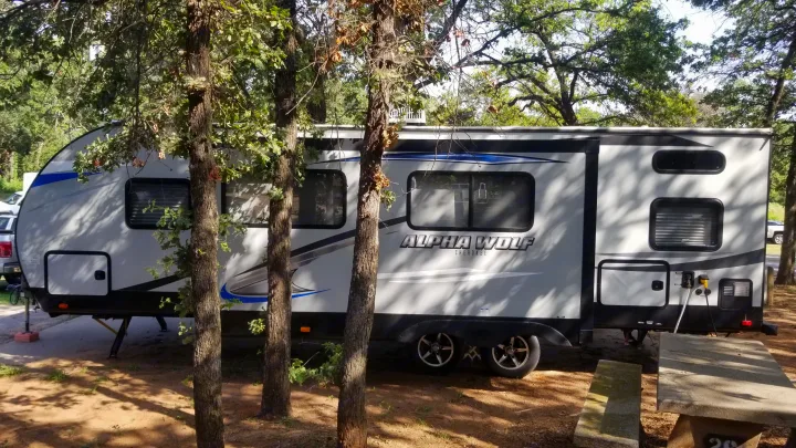 Modern gray Alpha Wolf Cherokee RV rental parked at a wooded campsite with a picnic table, ready for a serene outdoor adventure.. Forest River Cherokee Alpha Wolf 2020