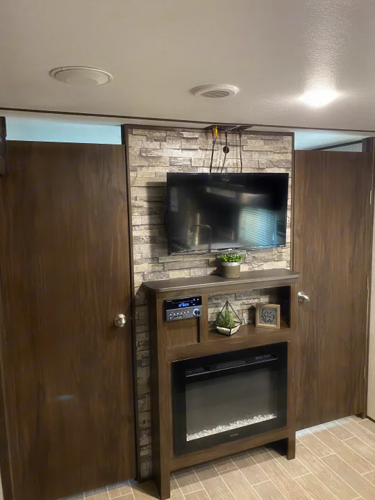 RV rental interior featuring a cozy entertainment center with TV, fireplace, and stereo, flanked by two wooden doors.. Forest River Cherokee Alpha Wolf 2020