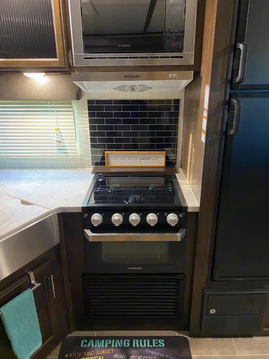 An RV rental's sleek kitchen featuring Furrion appliances (microwave, stove, oven, hood) and a subway tile backsplash.. Forest River Cherokee Alpha Wolf 2020