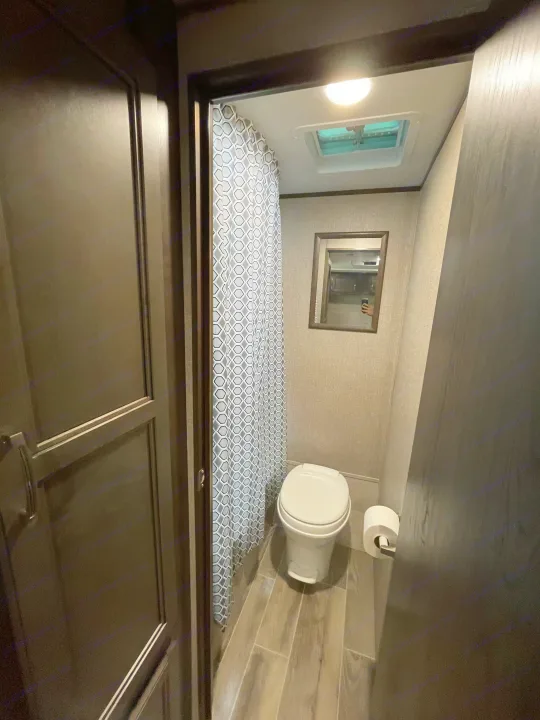 This RV rental bathroom features a toilet, shower with patterned curtain, mirror, and skylight for a comfortable travel experience.. Jayco Jay Flight 2021
