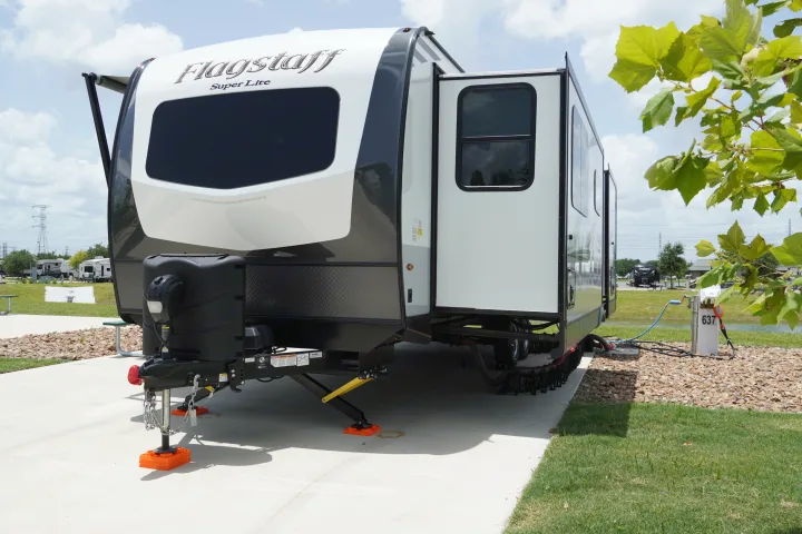 A white and black Flagstaff Super Lite travel trailer, a common RV rental, parked on concrete with hookups at a sunny campsite.. Forest River Flagstaff Super Lite 2021