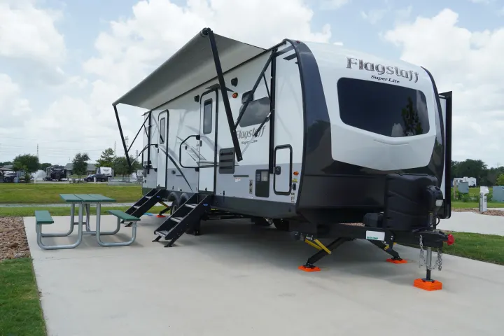 A white Flagstaff Super Lite RV rental parked on a concrete pad at a campground, with an awning extended & picnic table.. Forest River Flagstaff Super Lite 2021