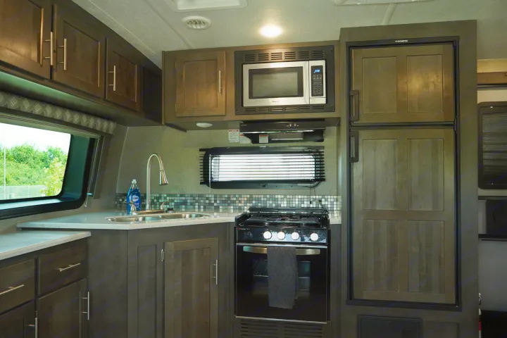 Modern RV rental kitchen: features a microwave, gas stove, large refrigerator, sink, and dark wood cabinets.. Forest River Flagstaff Super Lite 2021