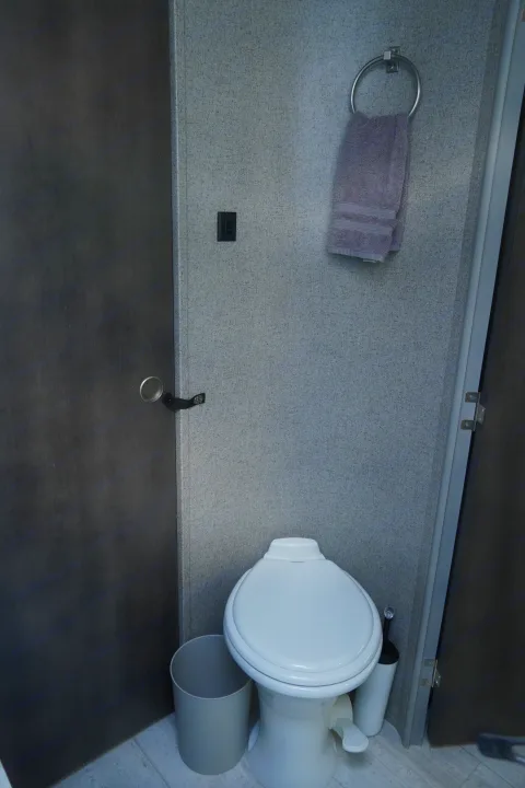 Compact RV rental bathroom: a white toilet, gray trash bin, and a purple towel on the wall. Space-saving design for travel.. Forest River Flagstaff Super Lite 2021