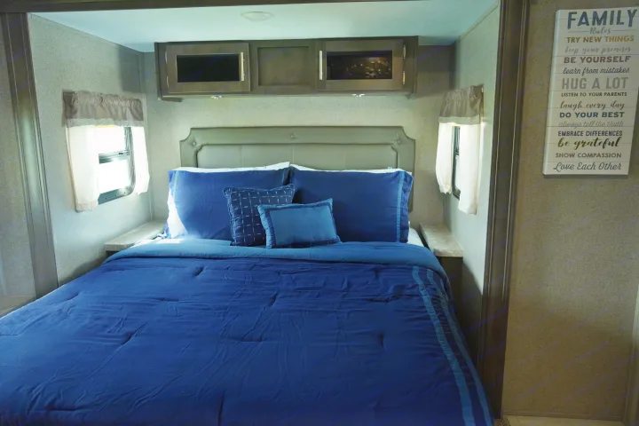 Interior of an RV rental bedroom: cozy blue bed, side windows, overhead cabinets, and a 'Family Rules' wall sign.. Forest River Flagstaff Super Lite 2021