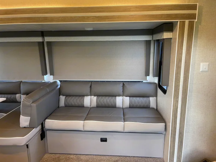Experience comfort in this modern gray sofa and dinette seating area inside your RV rental, featuring pull-down blinds and stylish lighting.. Forest River Wildwood 2021
