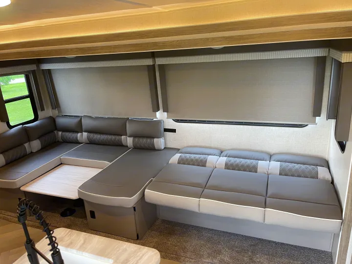 Inside an RV rental: a modern U-shaped lounge and dining area with comfortable grey cushions and large windows.. Forest River Wildwood 2021