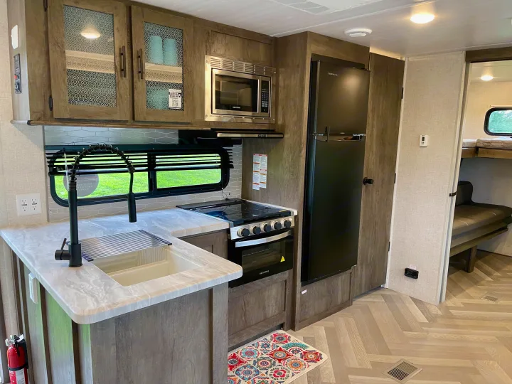 Spacious RV rental interior with a modern kitchen (sink, stove, microwave, fridge) and bunk beds visible in the back.. Forest River Wildwood 2021