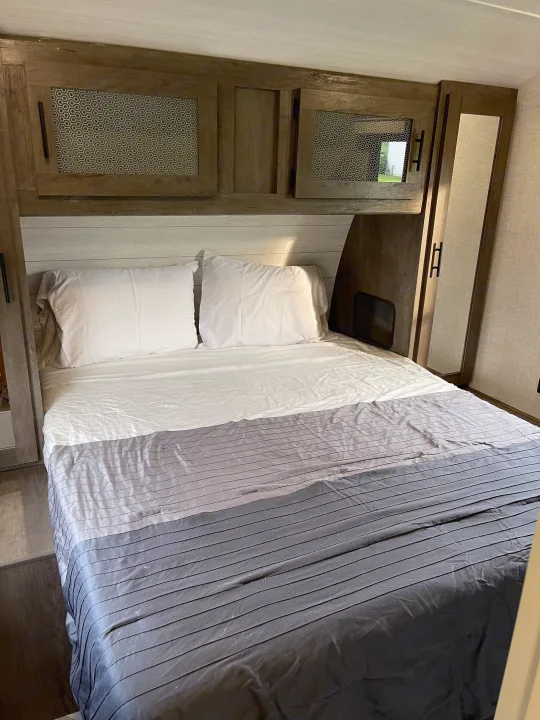 Cozy RV rental bedroom featuring wood cabinets with honeycomb accents, mirrored storage, and a comfy bed with striped bedding.. Forest River Wildwood 2021