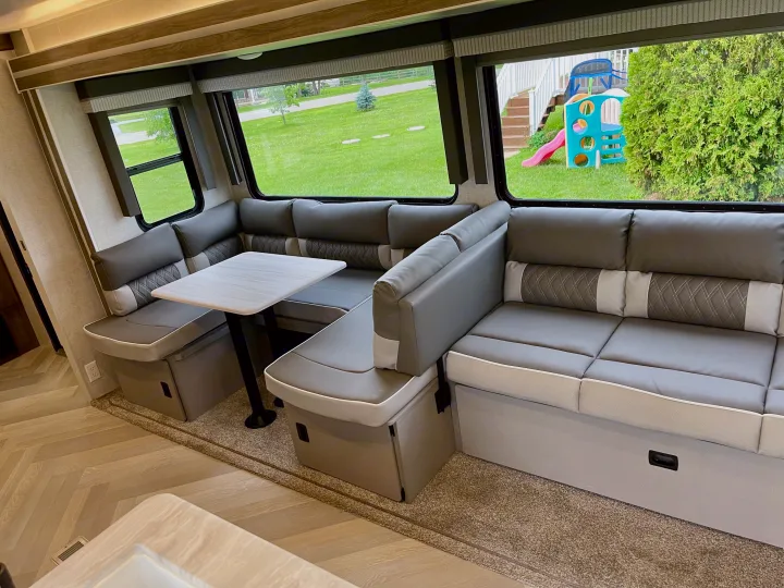 Inside this RV rental, an L-shaped dinette with a table offers comfortable seating. Windows show a grassy yard and kids' slide.. Forest River Wildwood 2021