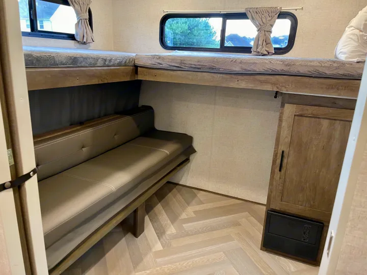 Modern RV rental interior: L-shaped bunk beds, cozy dinette, windows, and light flooring create a functional space.. Forest River Wildwood 2021