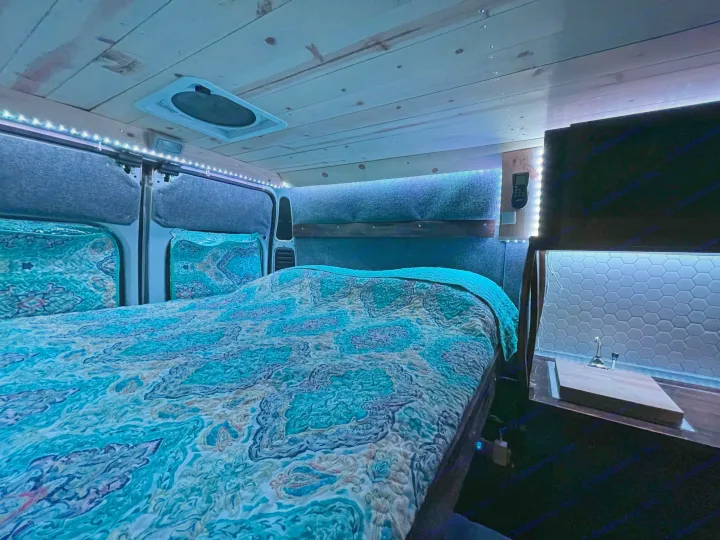 Inside this cozy RV rental: a comfortable bed with ambient blue lighting and a compact kitchen area.. Ram Promaster 2020