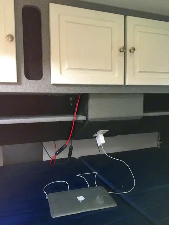 RV rental interior: A MacBook charging on blue cushions, with custom shelves and a visible power setup.. Little Guy Other 2011