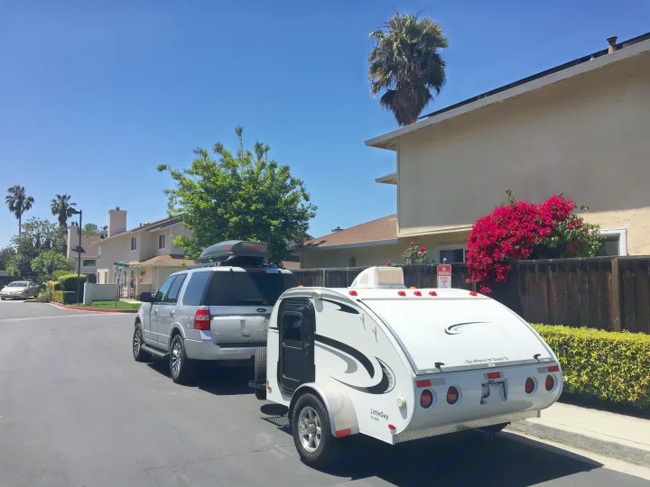 Silver SUV towing a white "Little Guy Six Wide" teardrop camper, possibly an RV rental, on a sunny residential street.. Little Guy Other 2011