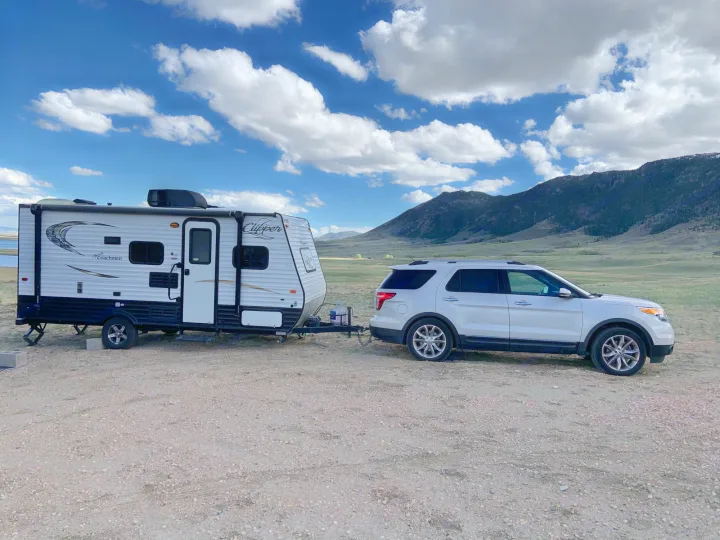White RV rental & SUV parked by a lake and mountains, perfect for camping. Enjoy nature's beauty on your next adventure.. Coachmen Clipper 2015
